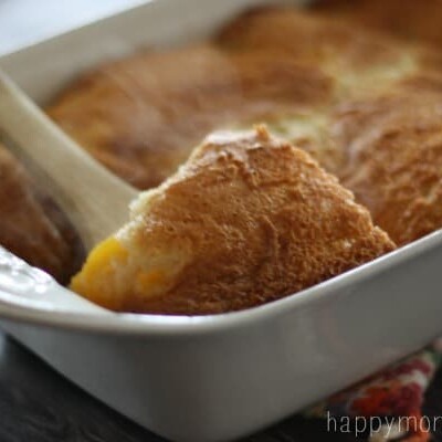 Spoon scooping peach cobbler from a baking dish.