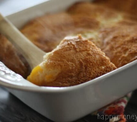 Spoon scooping peach cobbler from a baking dish.