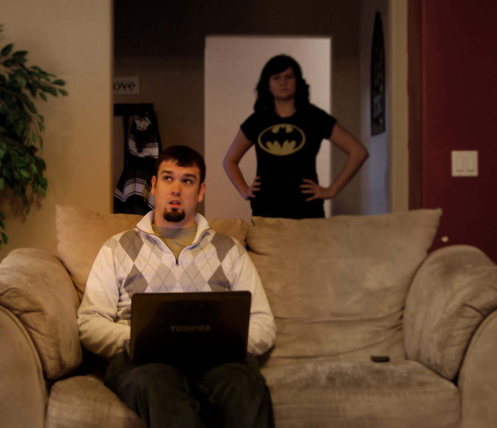wife wearing batman shirt with man on computer on the couch