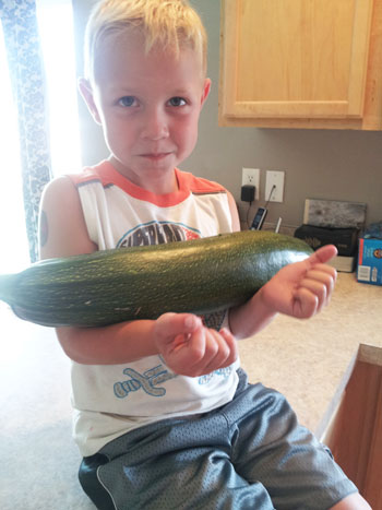 Child holding a large zucchini in his arms.