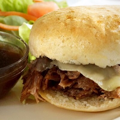 French dip sandwich on a plate with dip and salad.
