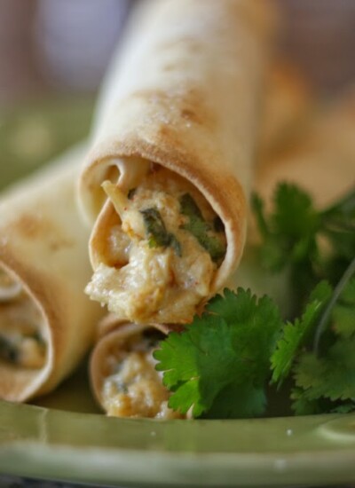 Pile of crispy chicken taquitos with cilantro and pepper-jack cheese.