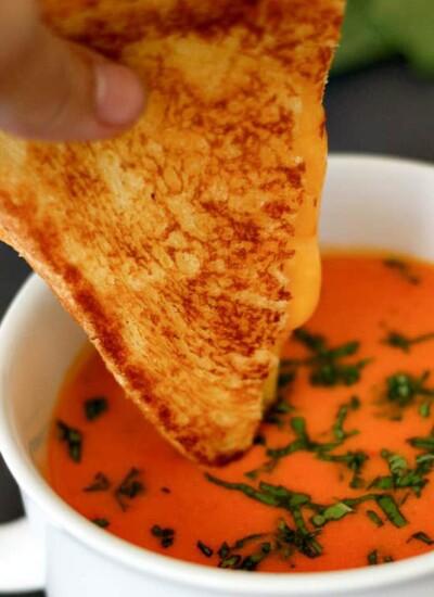 Person dipping a grilled cheese sandwich into a bowl of garden fresh tomato soup.