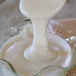 Marshmallow frosting pouring from a spoon into a glass container.
