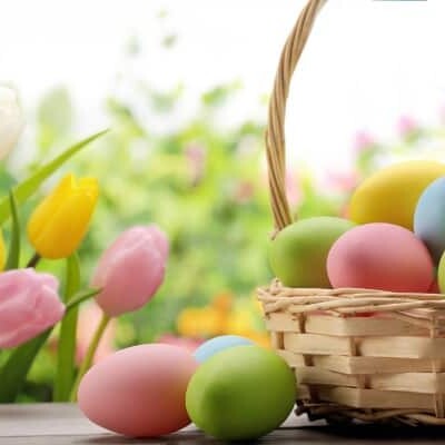 Pastel eggs in and around a basket with flowers.
