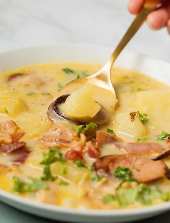 Zuppa Toscana soup in a white bowl with a spoon lifting out a bite with a potato on it. 