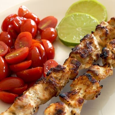 Garlic lime chicken kabobs on a plate with tomatoes and lime slices.