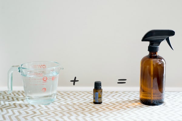 Measuring cup of water, jar of essential oil and a spray bottle.