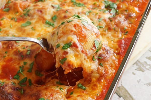 A glass pan with a metal fork holding a stuffed shell covered in cheese and herbs.