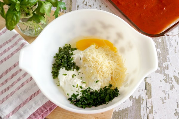 A white bowl with ingredients for stuffed shells in them - eggs, cheeses, and herbs.