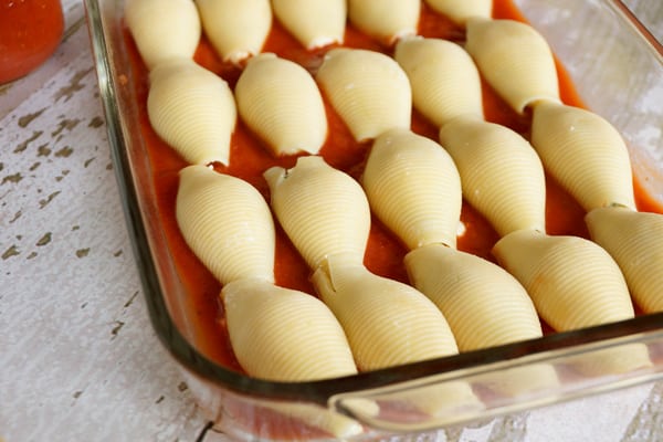 A glass pan with uncovered pasta shells in tomato sauce.