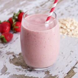 Strawberry oatmeal smoothie in a glass with a red and white straw.