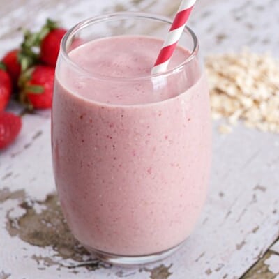 Strawberry oatmeal smoothie in a glass with a red and white straw.