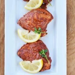 Baked Tandoori chicken on a serving dish with lemon slices.