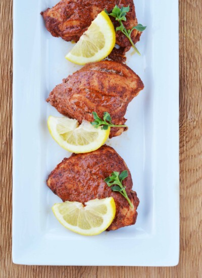 Baked Tandoori chicken on a serving dish with lemon slices.