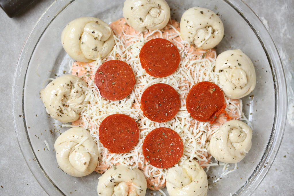 Cheese dip topped with pepperoni surrounded by rolls of pizza dough.