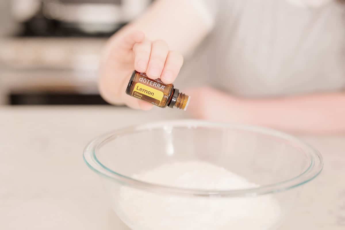 There is clear bowl with white powder in it with a hand pouring lemon essential doterra oil.