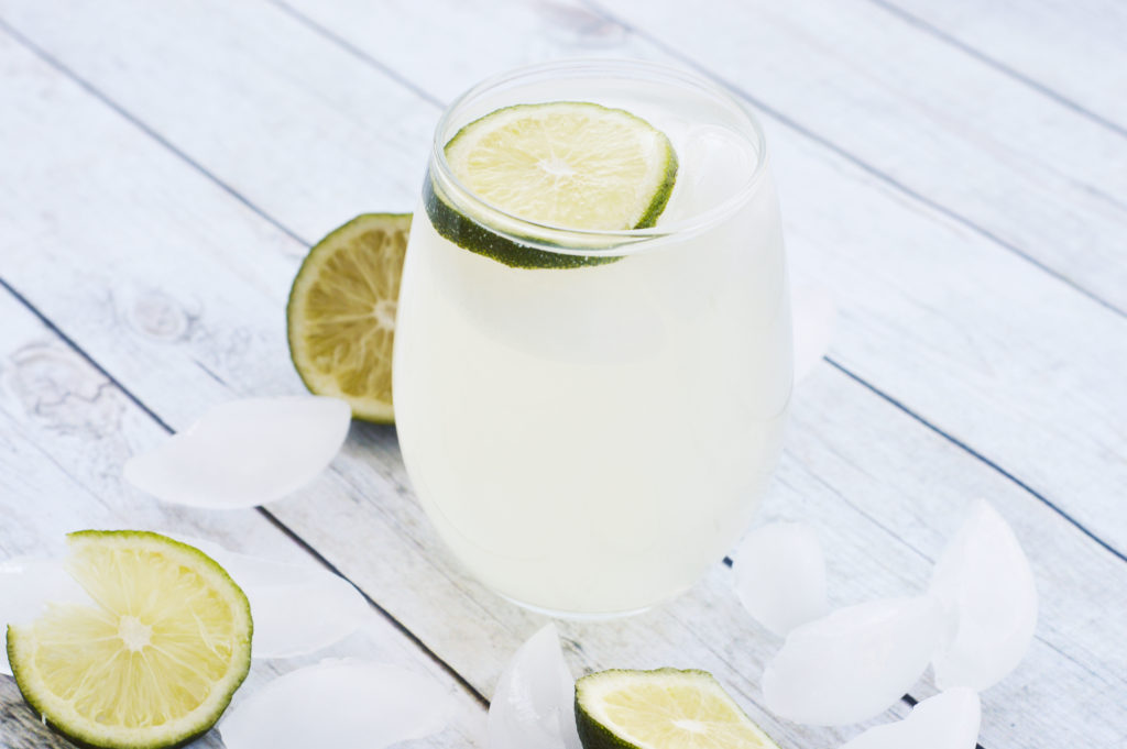 Glass of sparkling ginger limeade topped with a lime slice on a table with limes and ice.