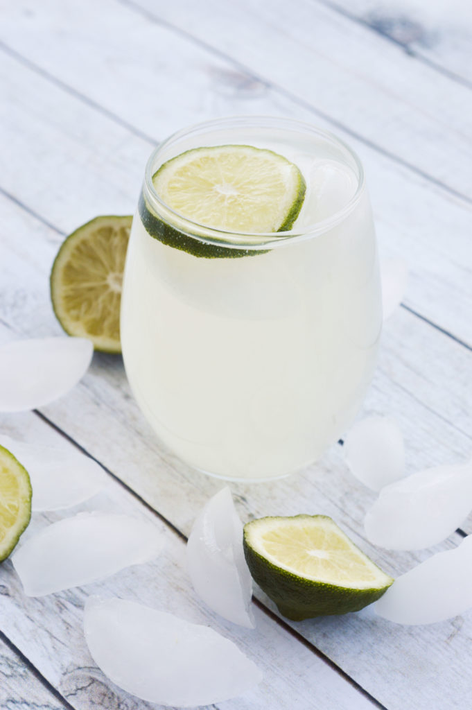 Glass of sparkling ginger limeade topped with a lime slice on a table with limes and ice.