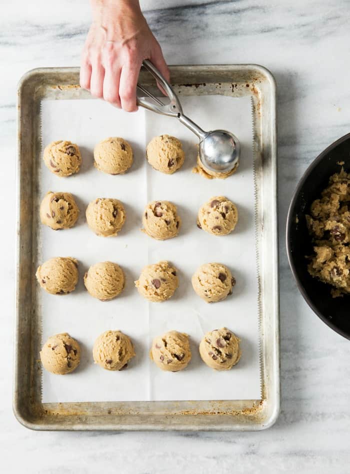 Ice cream scoop putting cookie dough on a lined baking sheet.