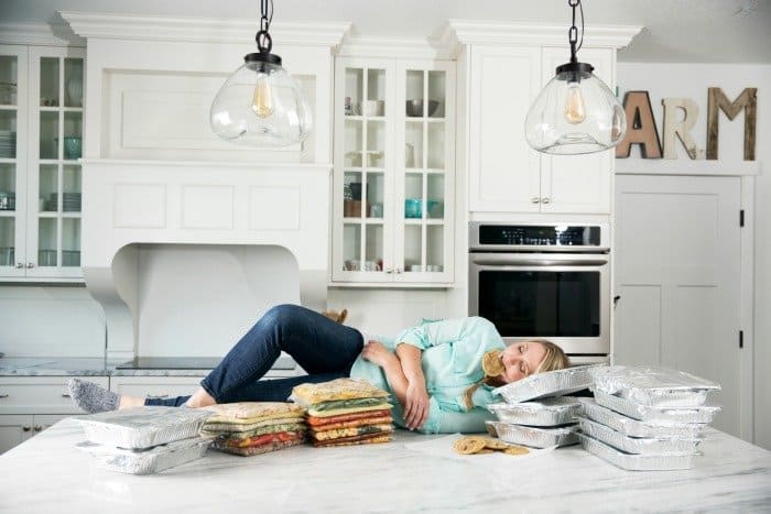 Karrie lying on a counter with freezer meals eating a cookie.