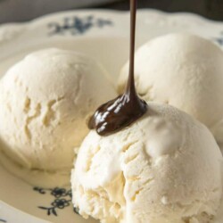 Chocolate drizzling onto scoops of no-churn homemade vanilla ice cream.