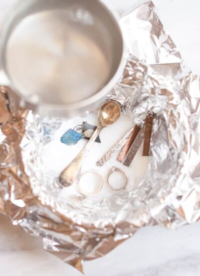 Measuring cup of water over an aluminum-foil-lined bowl of jewelry and cleaner.