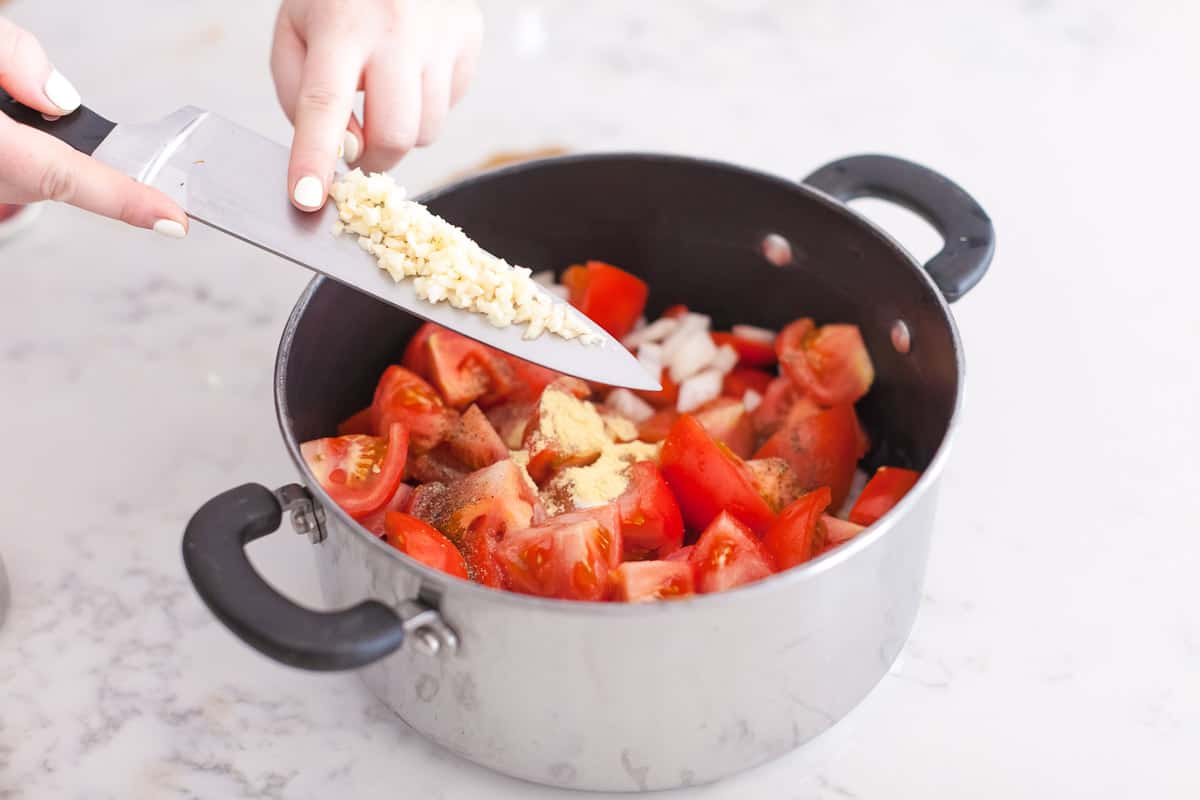 adding garlic to pot with chopped tomatoes