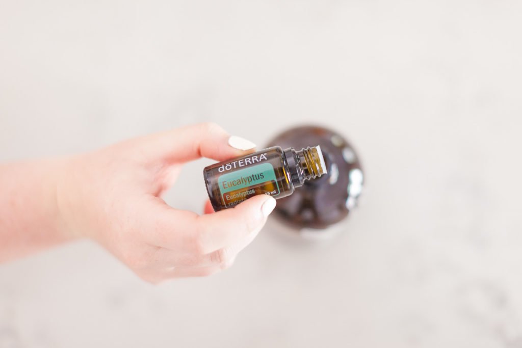 On a white background there is a hand pouring out from a Eucalyptus doterra essential oil bottle into a brown bottle.