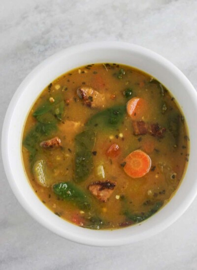 Sausage and spinach soup in a white bowl.