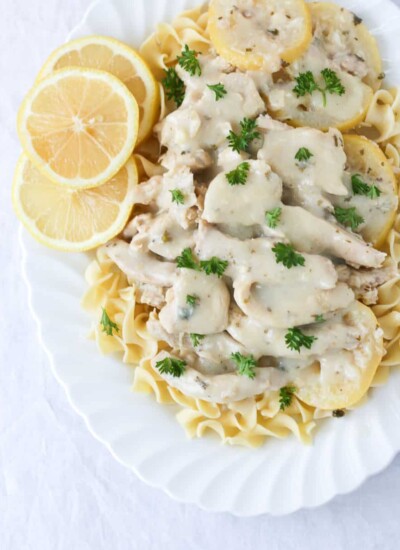 Country lemon chicken over pasta on a white serving dish.