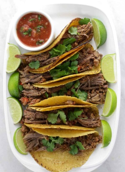 Shredded beef fajitas on a white tray with lime wedges and salsa.