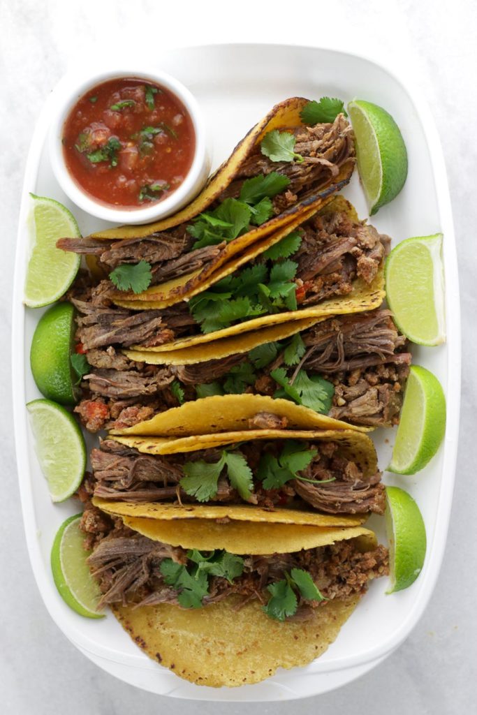 Serving platter of beef fajitas with salsa and lime wedges.