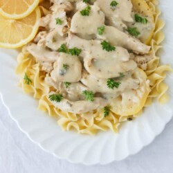 Country lemon chicken over pasta on a white serving dish.