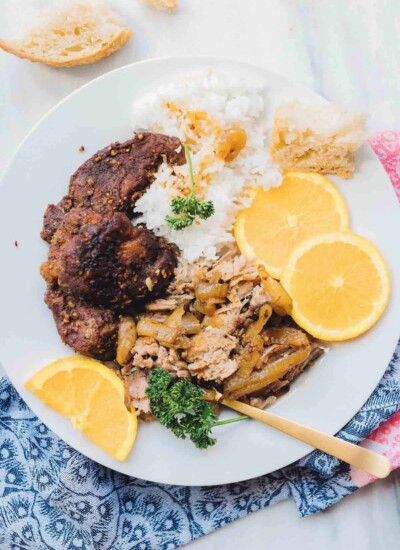 Orange spiced pork on a plate with rice and lemon slices.