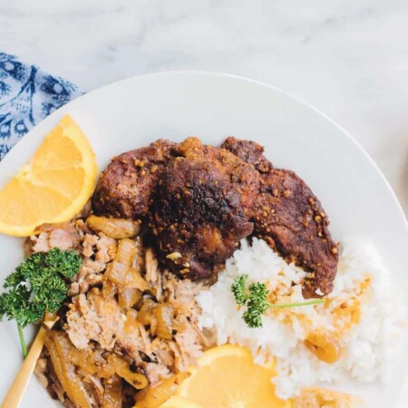 Orange spiced pork on a plate with rice and lemon slices.