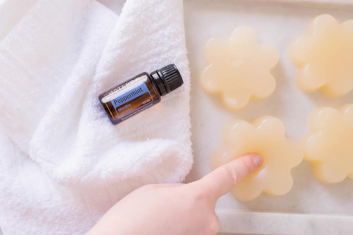 Person poking a flower-shaped shower jelly next to a bottle of doTerra peppermint essential oil.