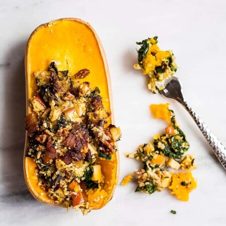 Fork next to a stuffed butternut squash with bacon, apples, and pecans.