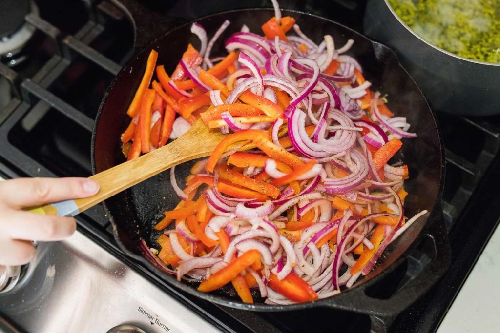 onions and bell peppers frying in a pan.