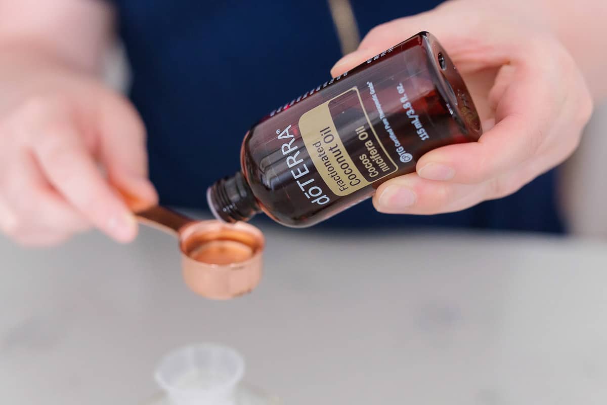 A hand pouring fractionated coconut oil into the measuring spoon.