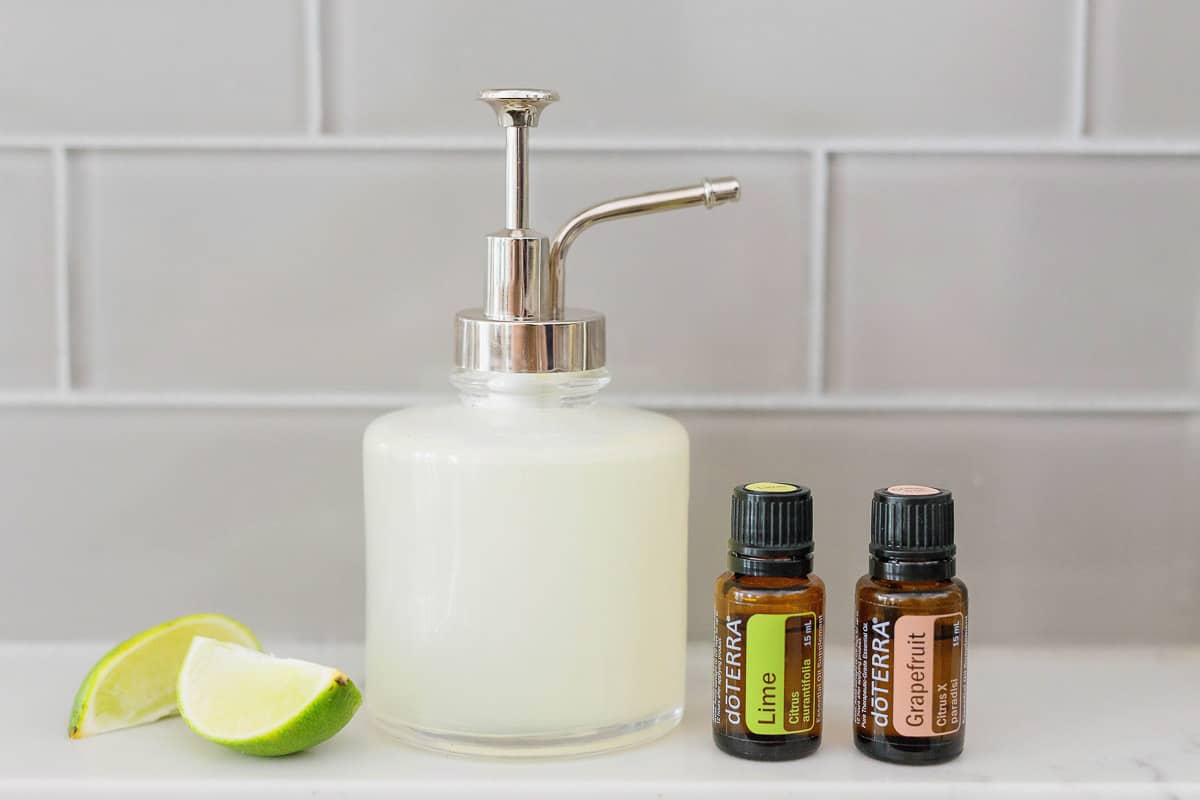 Two cut limes next to a white soap canister with two doterra essential oil bottles on a white counter.