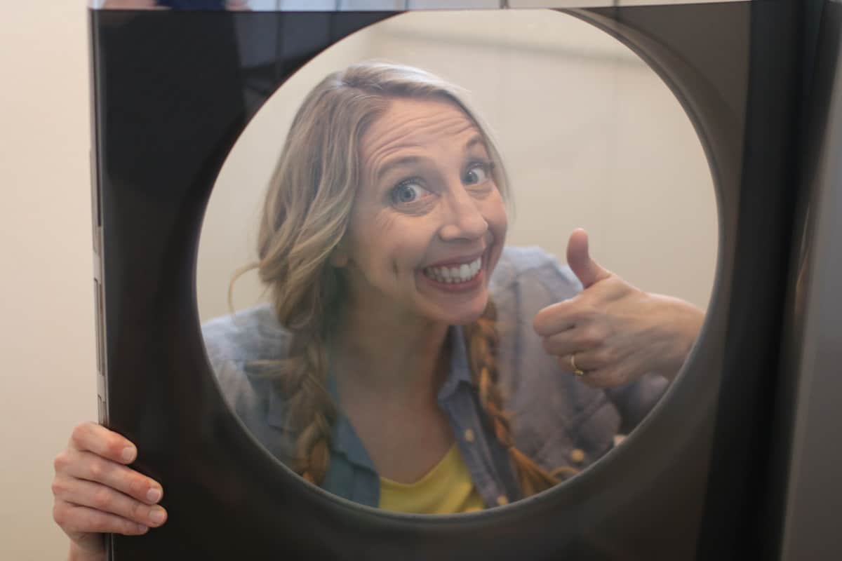 Karrie smiling and giving a thumbs up through the window of her Maytag washer.