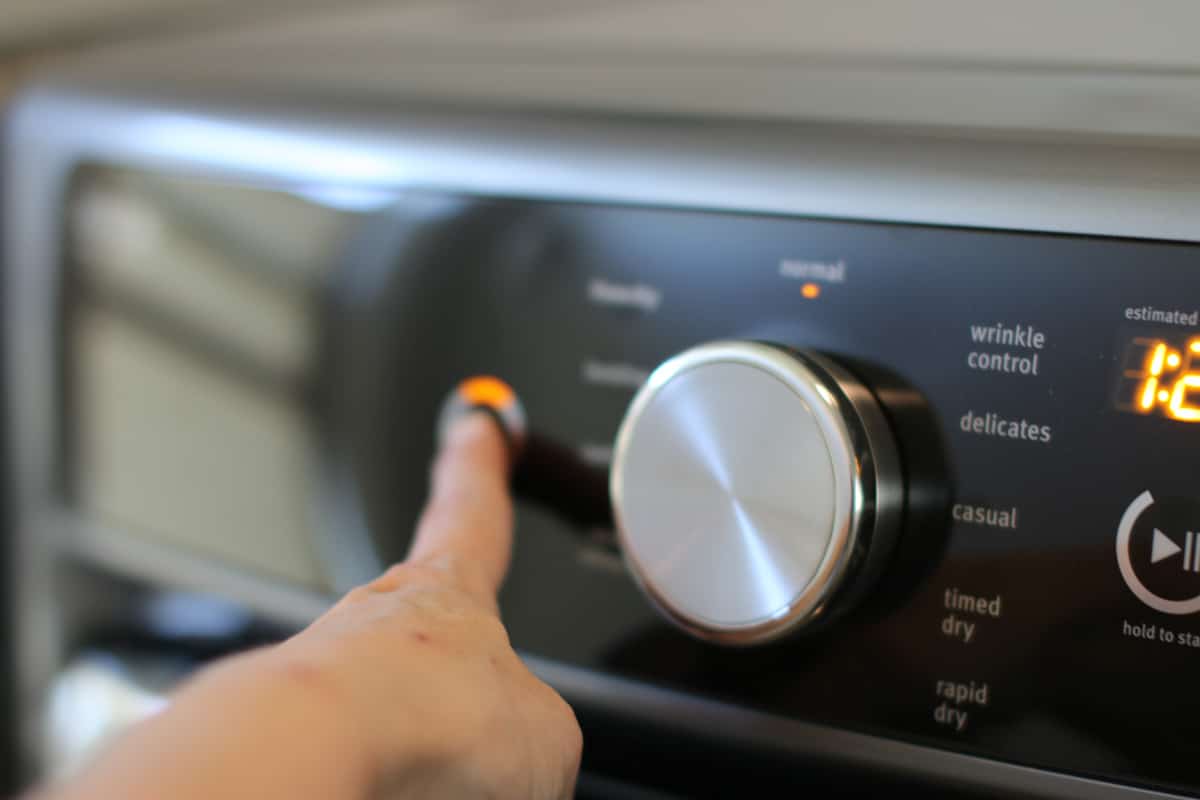 Person pushing a button on a Maytag dryer.