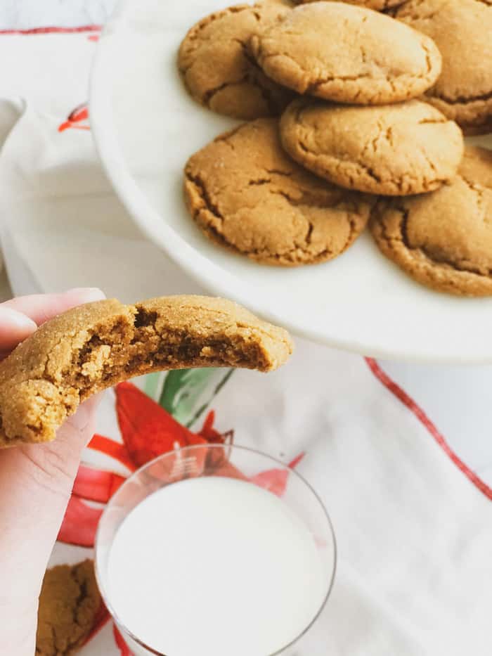 bite out of a chewy ginger molasses cookie with a plate of cookies and milk