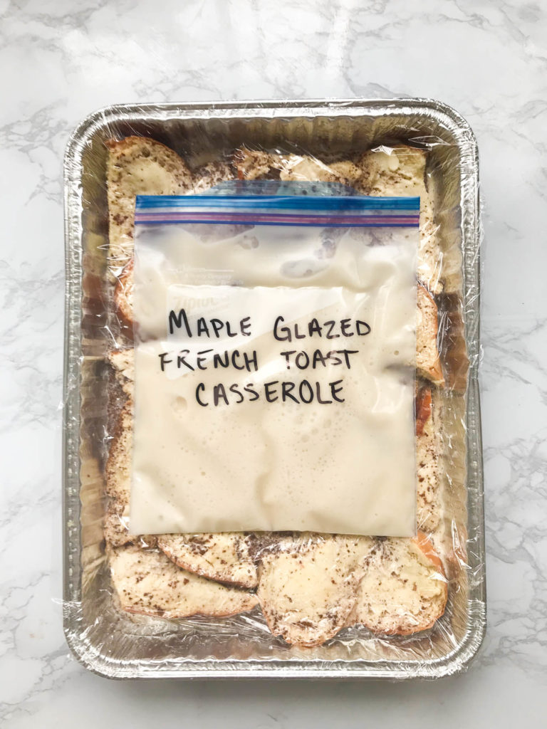 A foil pan with french toast in it covered in plastic wrap with a resealable bag full of white icing with the words Maple Glazed French Toast Casserole on it.