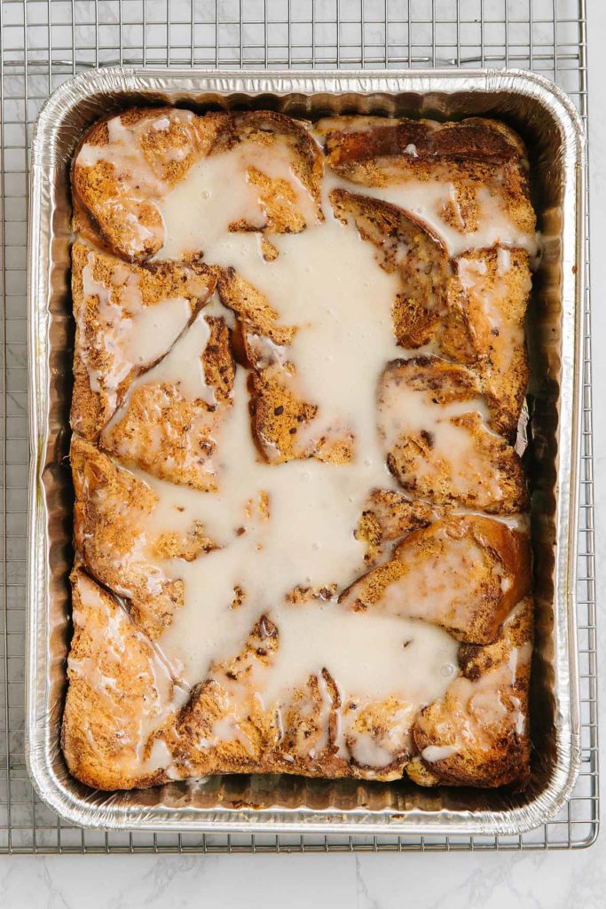 A foil pan full of breakfast casserole with icing on top. It is sitting on a wire tray.