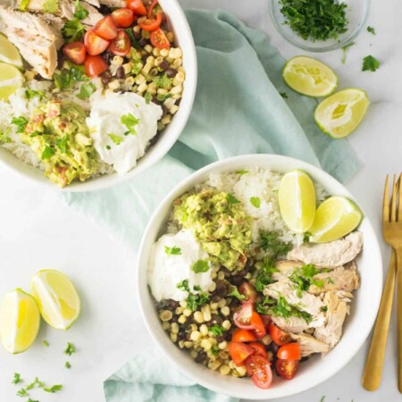 Bowls of cilantro lime chicken with tomatoes, limes, rice, and more.