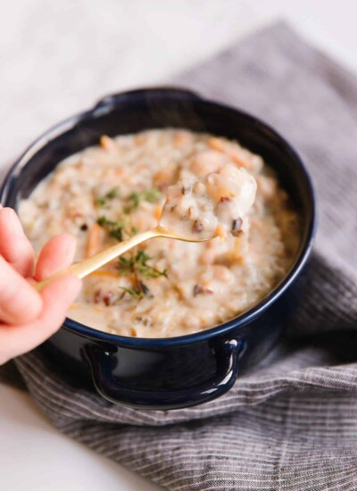Person using a golden spoon to scoop chicken wild rice soup from a bowl.