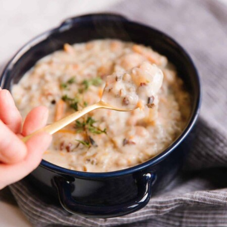 Person using a golden spoon to scoop chicken wild rice soup from a bowl.