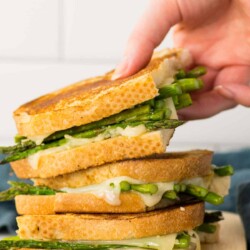 Person grabbing an asparagus grilled cheese from a stack of sandwiches.